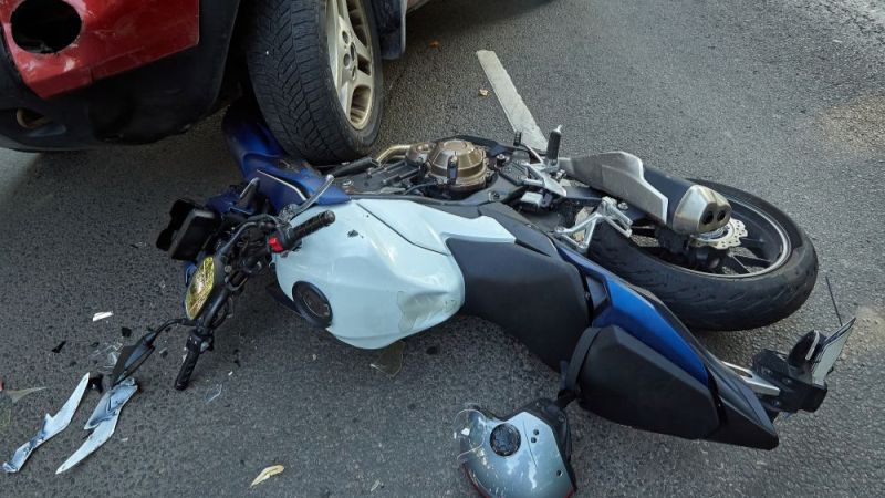 Motorcycle accident with a car on road, helmet and debris scattered around.